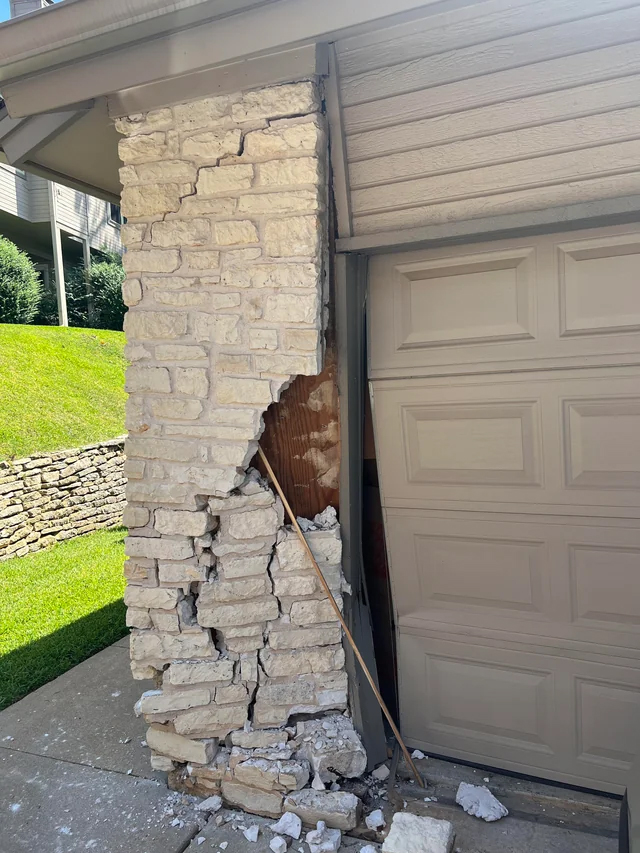 Damage to exterior stone wall of a residential garage due to a car hitting the garage.