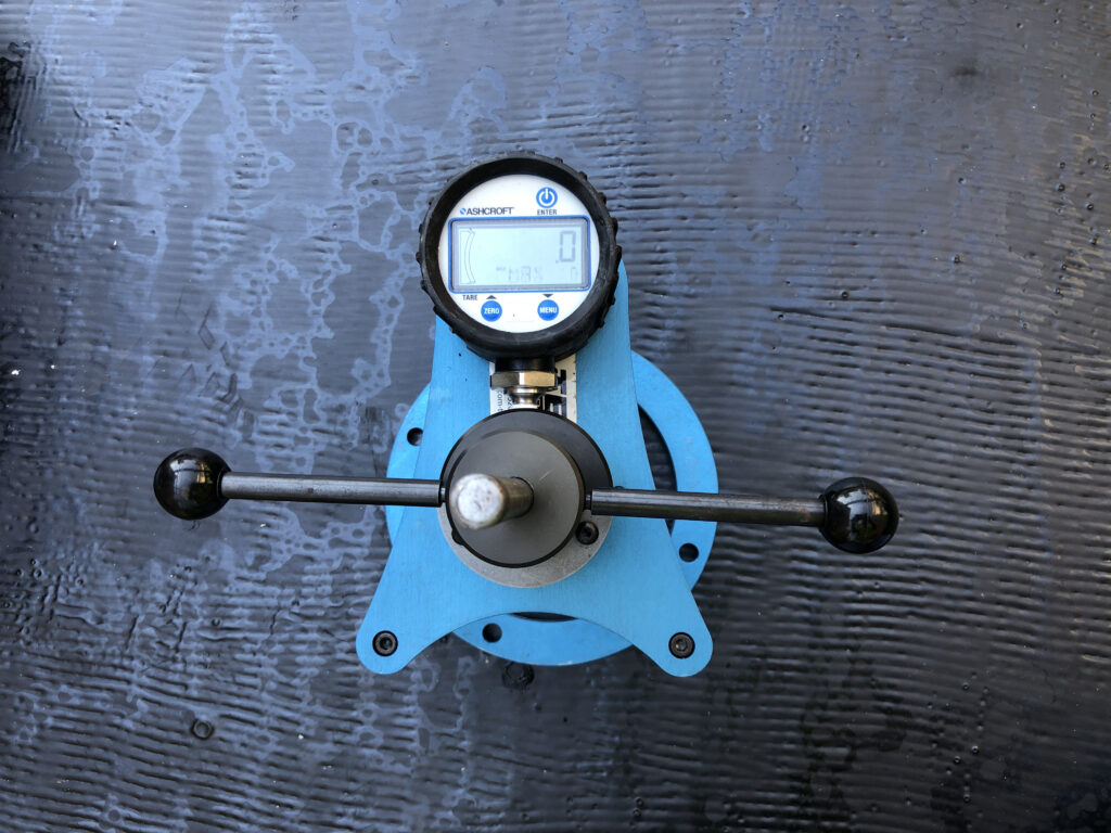 Ashcroft pull-off adhesion tester mounted on a dark waterproofing membrane.