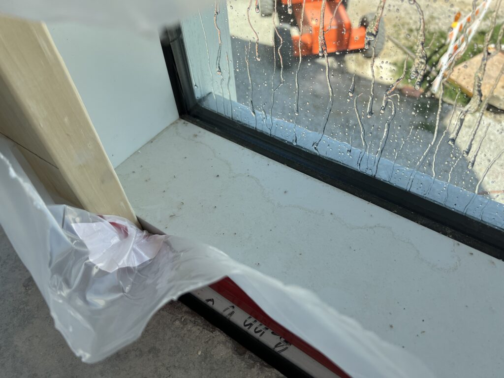 Water beading and running down the exterior of a curtainwall unit during spray testing, seen from inside at the sill.
