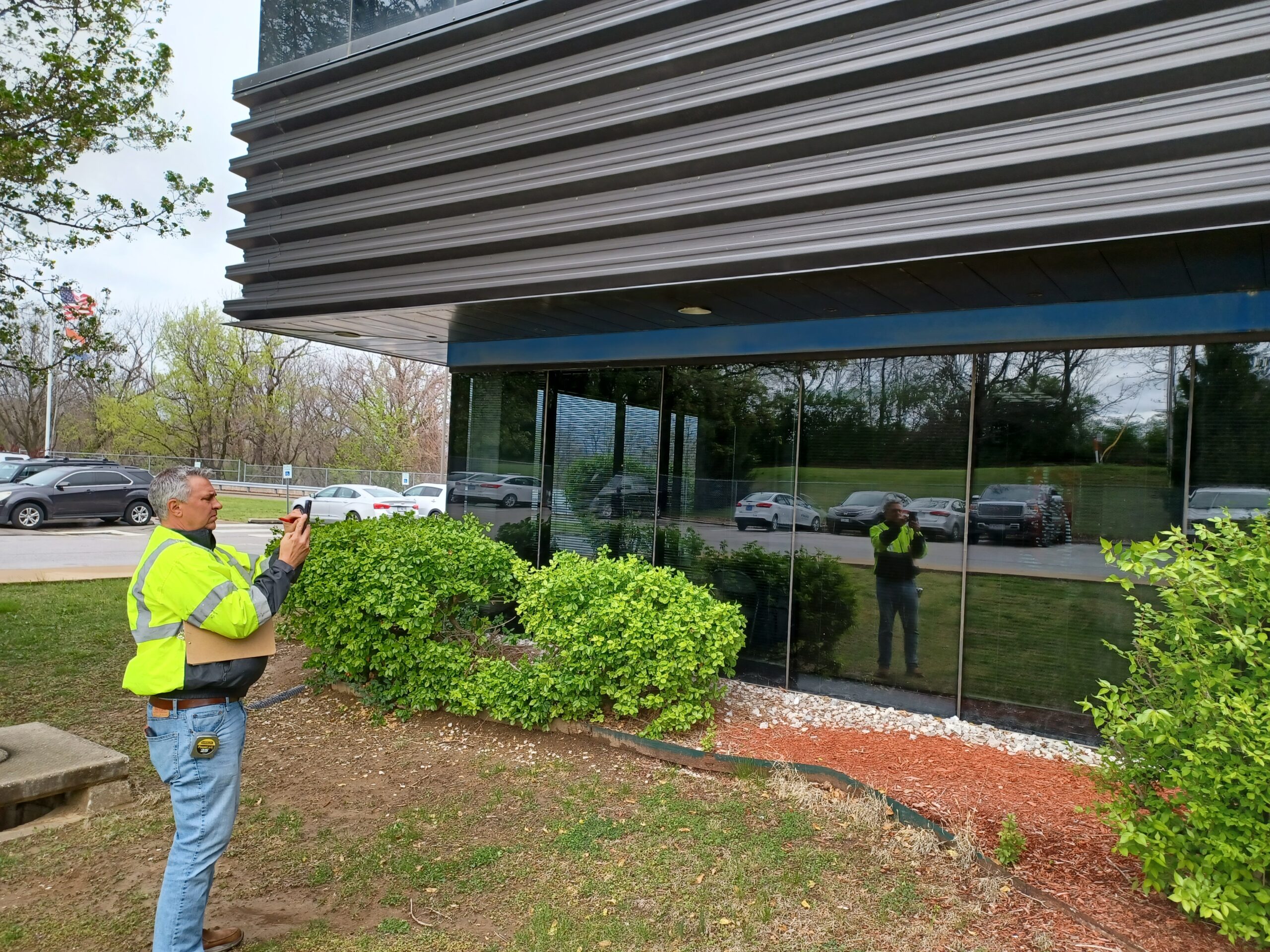 A team member in a hi-vis vest photographs the ribbon curtainwall during exterior observation.