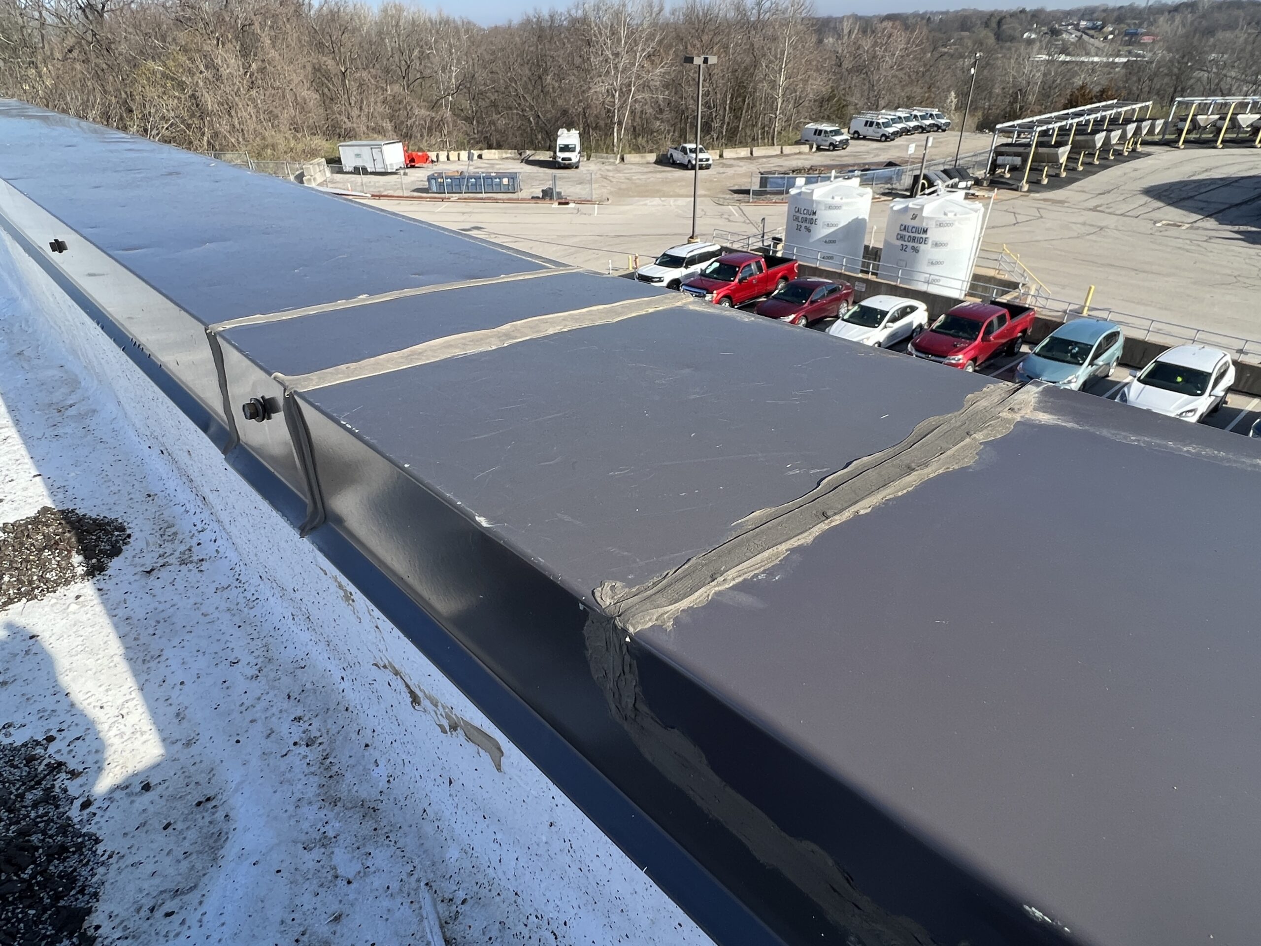 Metal coping and roof membrane along the parapet edge above the building's parking area.