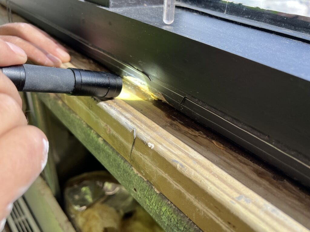 A flashlight held against the base of a window frame to inspect the joint during investigation.