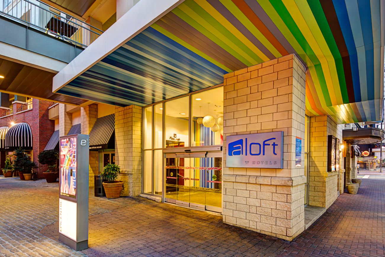 A vibrant, multi-colored striped overhead canopy and contemporary loft-inspired architecture outside hotel entrance.