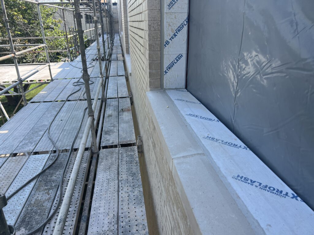 Close-up of window perimeter with Textroflash flashing membrane and a WRB installed, scaffold alongside.