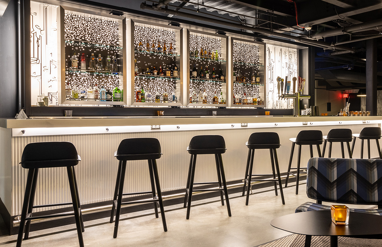 Bar inside Aloft hotel with stools and illuminated wall behind bara