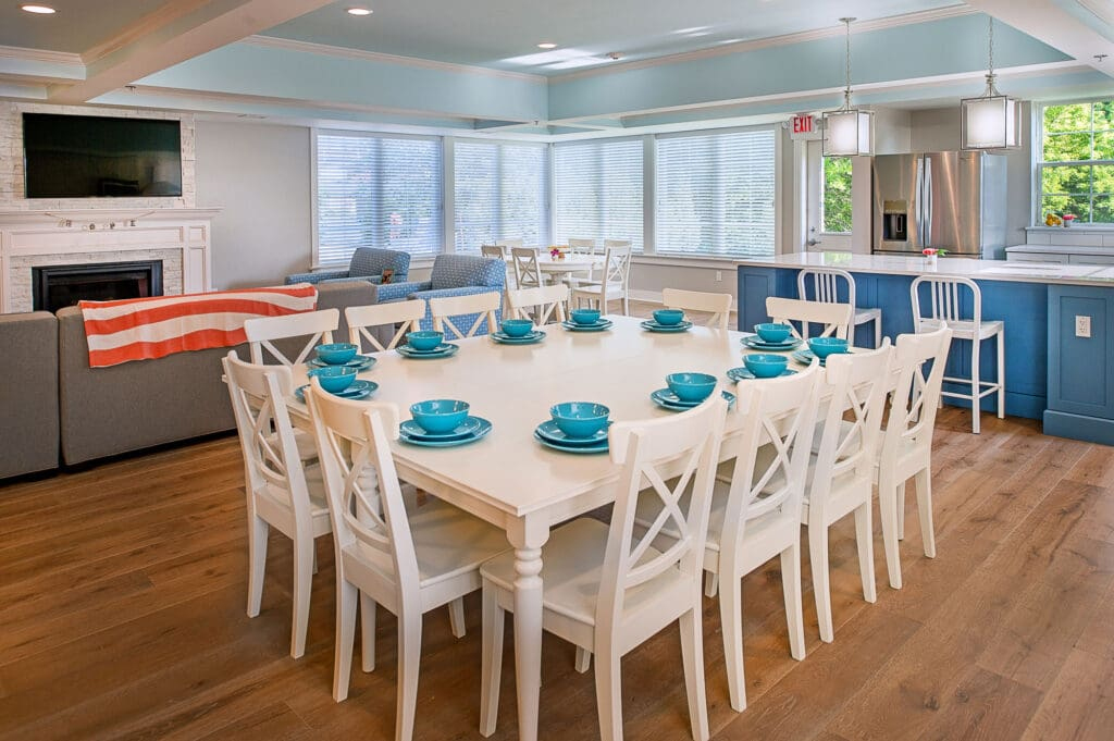 This spacious residential home features a large square dining table surrounded by classic white wooden chairs and set with bright turquoise bowls.