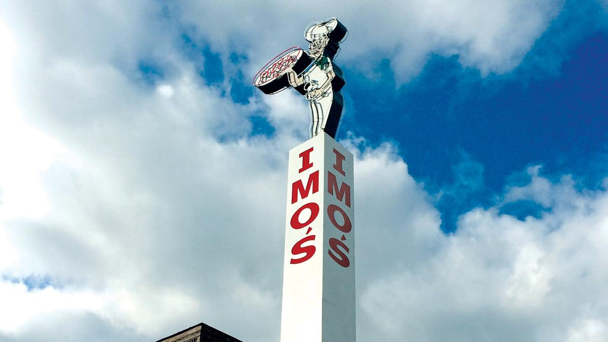White tall post sign with imo's pizza traditional pizza man logo on the top with a blue sky behind