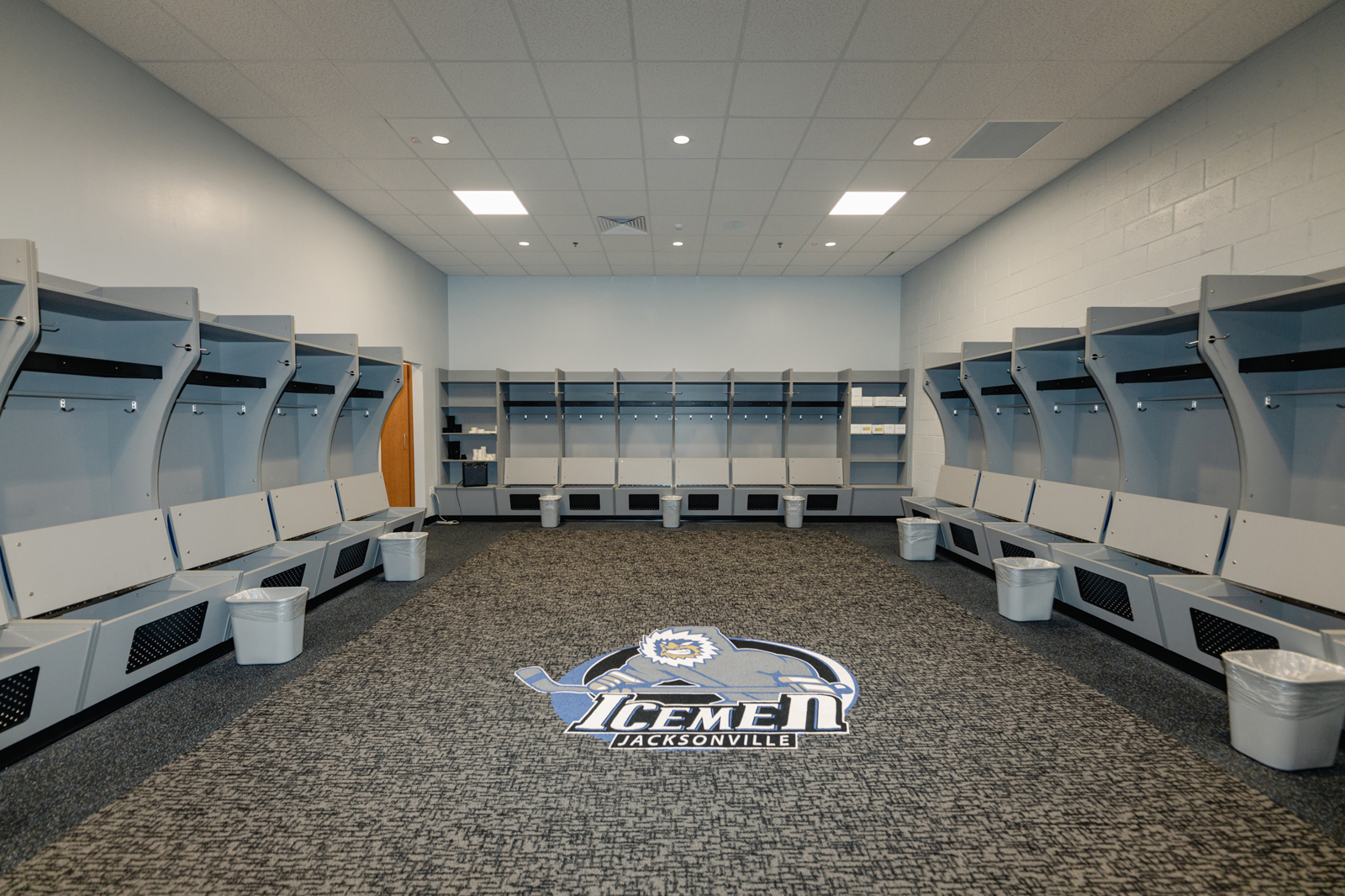 Inside hockey team lockker room with white lockers lining the wall and the team logo in the center of the carpet