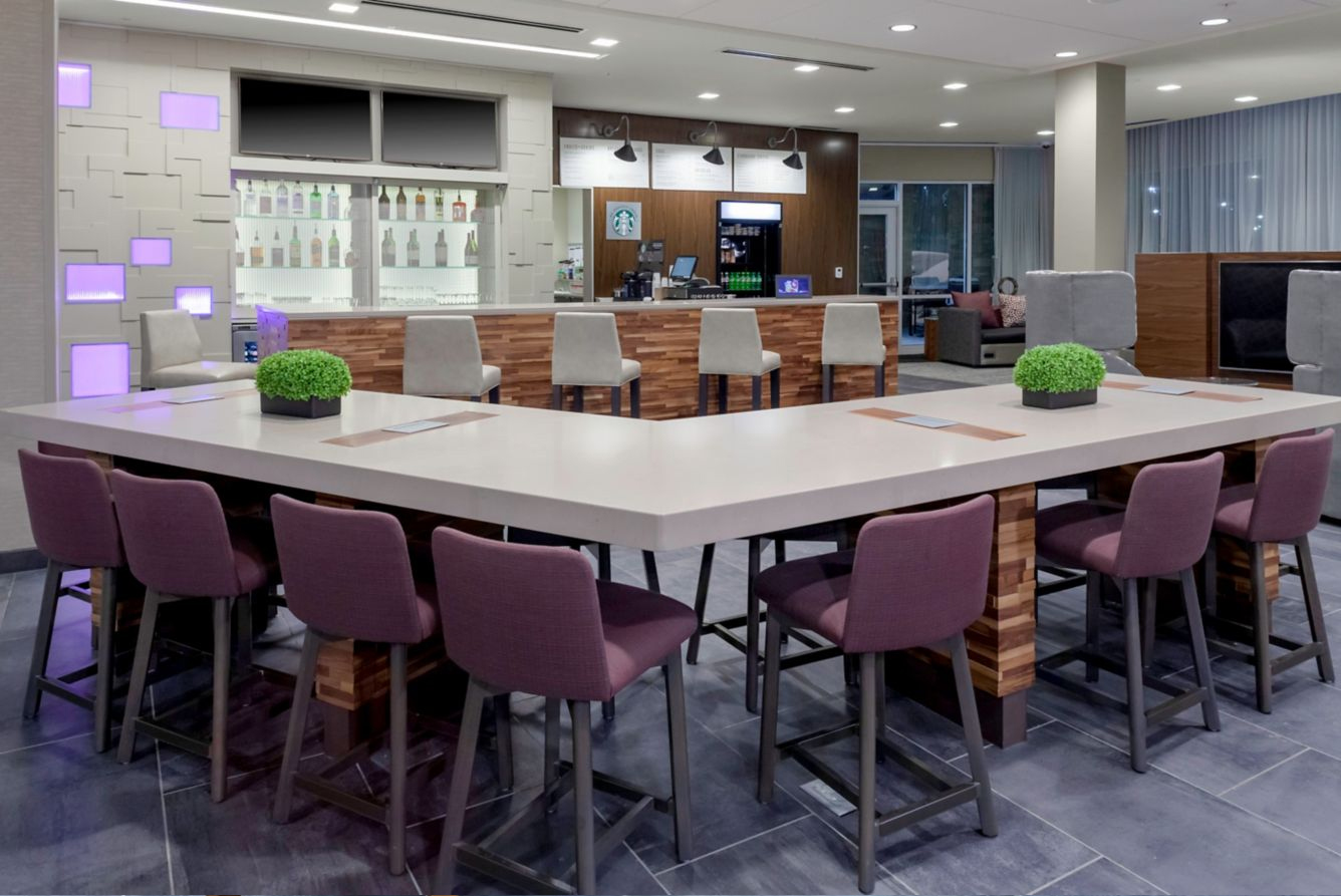 Bar area with white countertop and purple chairs inside hotel lobby.