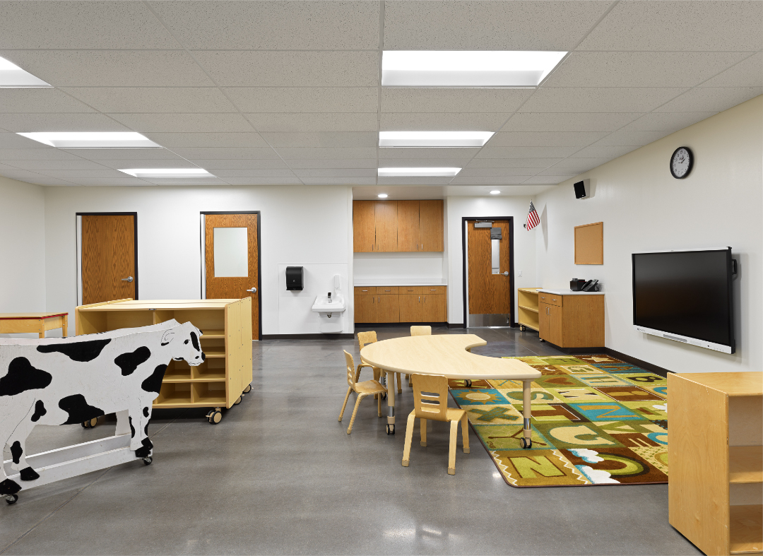 White walled classroom with little wooden table and chairs and colorful childish carpet