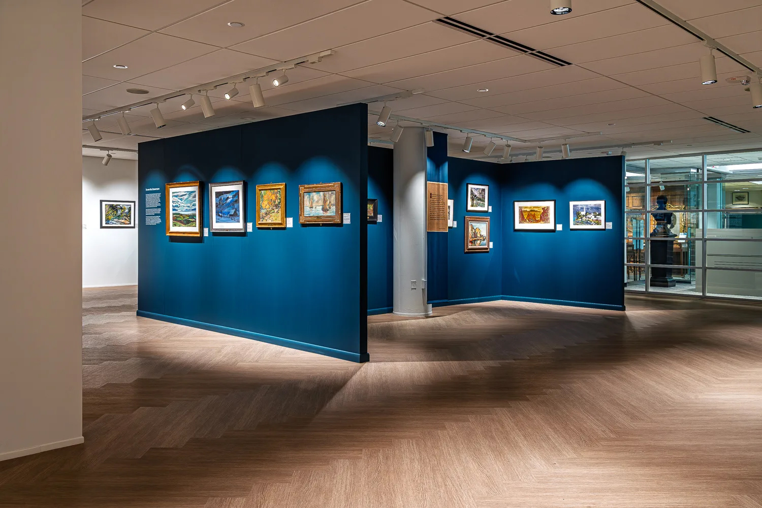 Art gallery at the St. Louis Mercantile Library with dark blue freestanding display walls, framed paintings, and track lighting over wood-look flooring.