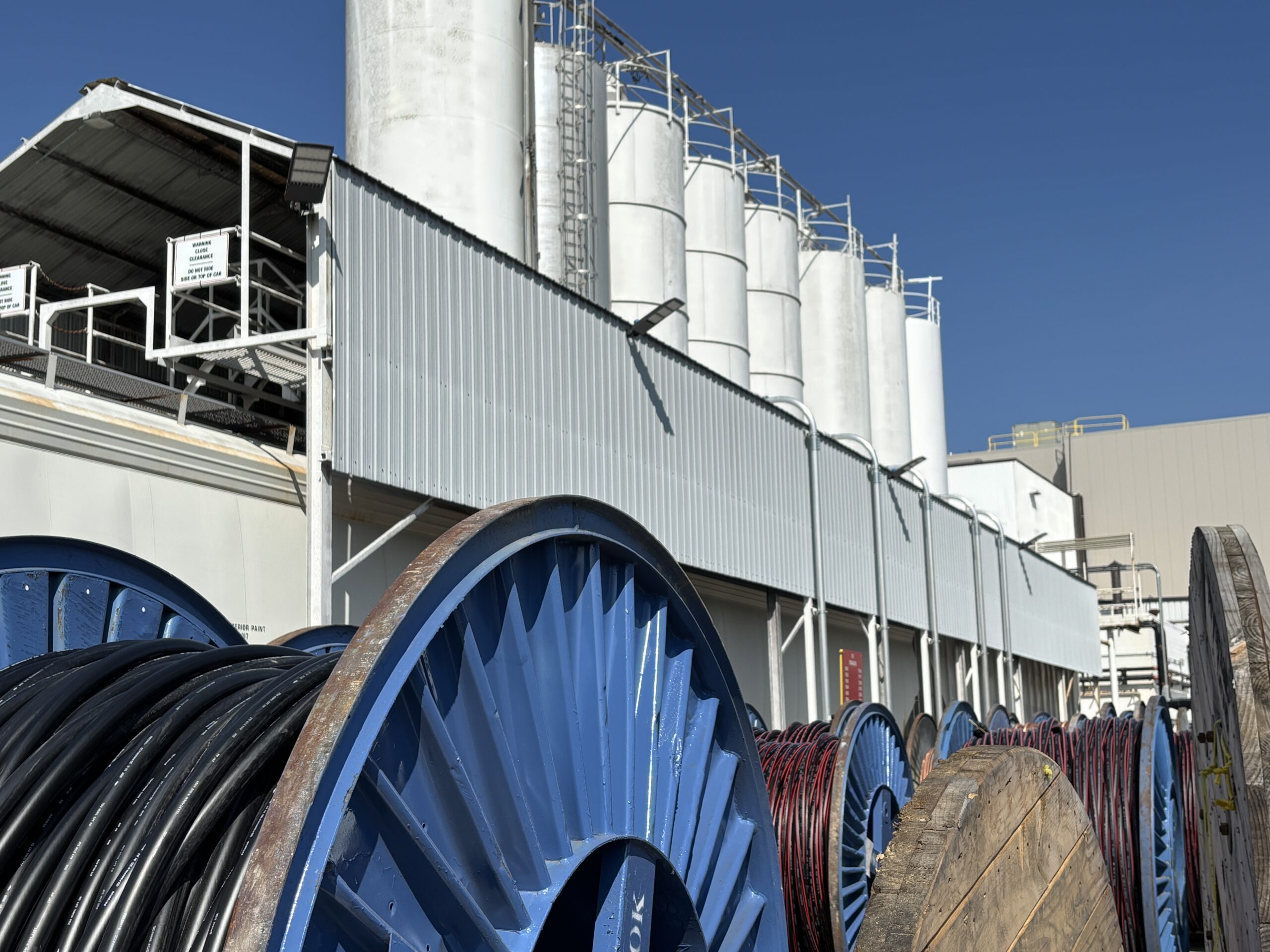 Cable reels staged outside the Prysmian plant in Du Quoin, Illinois, with storage silos and process structures behind.