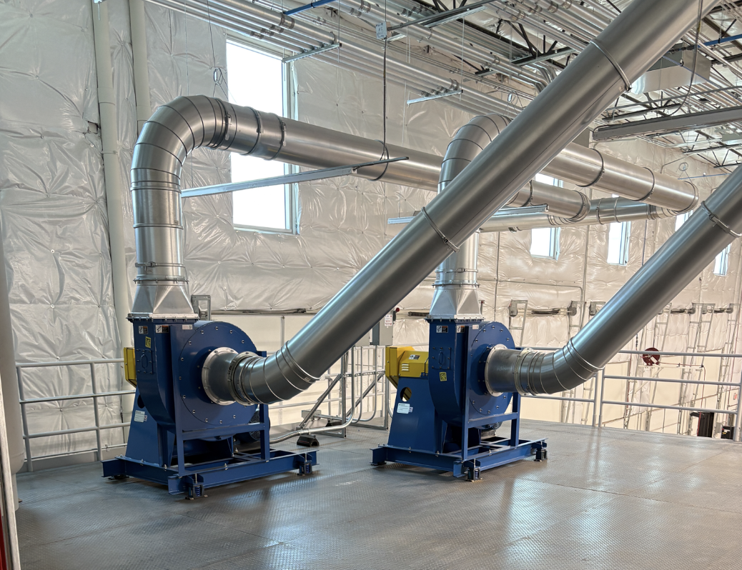 Two blue industrial dust collection blowers with large-diameter ducted runs on the mezzanine of the Zelis facility.