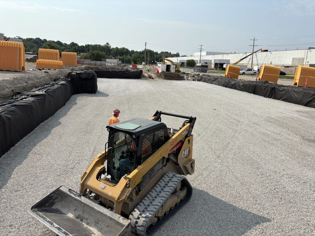 Skid steer grading the stone base for an underground stormwater detention system at the Enterprise loading dock site.