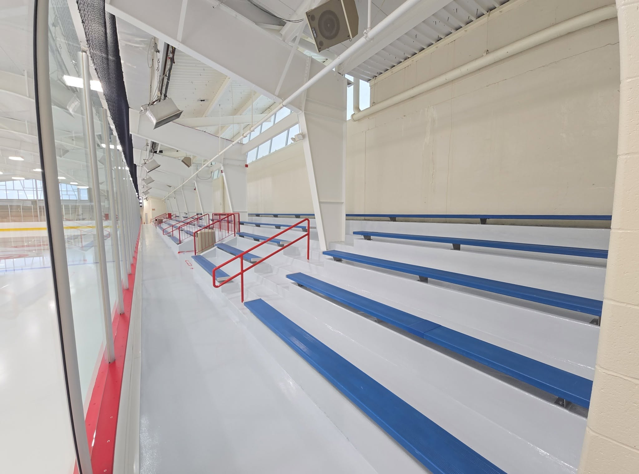 Spectator bleachers with blue seating stripes and red railings beside the glass at the renovated Kirkwood ice rink.