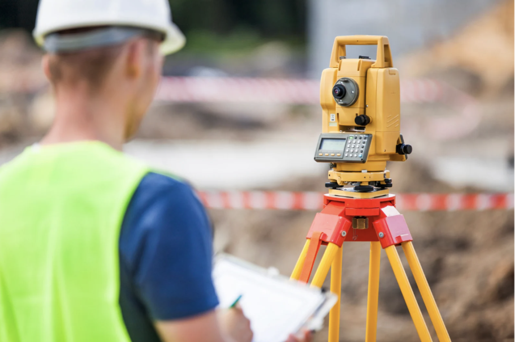 Land surveyor in a safety vest taking notes beside a total station on a construction site