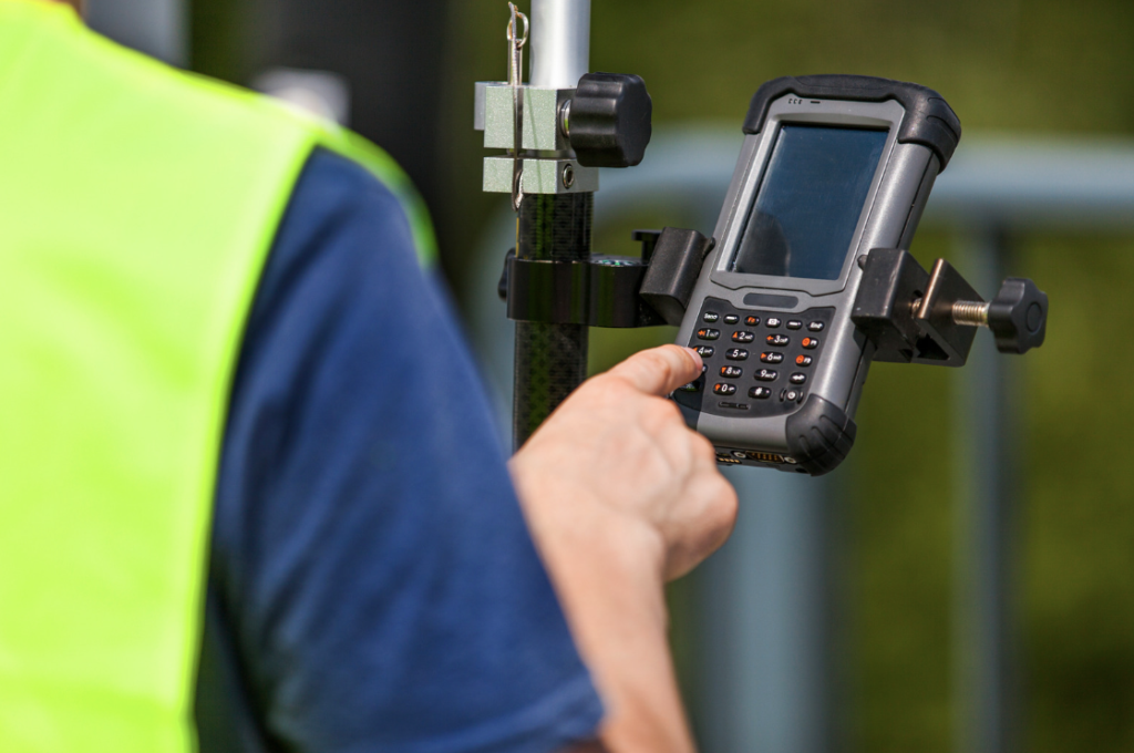 Surveyor entering data on a handheld GPS controller mounted to a survey pole in the field
